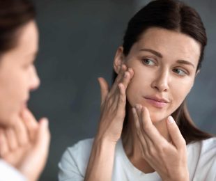 Close up unhappy sad woman looking at red acne spots on chin in mirror, upset young female dissatisfied by unhealthy skin, touching, checking dry irritated face skin, skincare and treatment concept